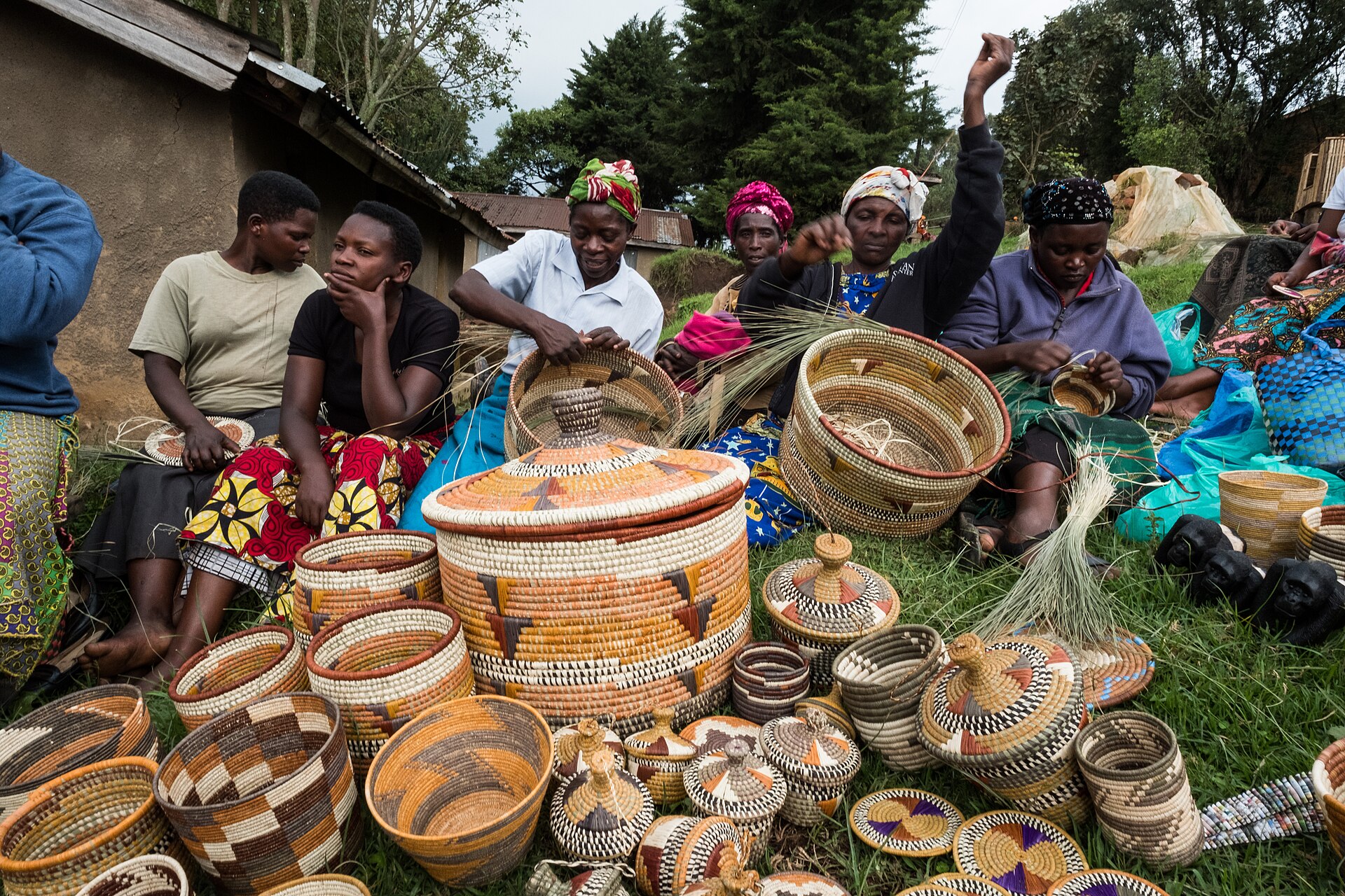 Women sitting on the grass weaving baskets, with many finished woven baskets laid out in front of them.
