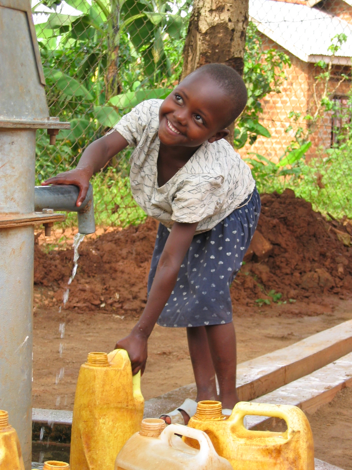 A smiling girl filling yellow jerrycans from the spout of a village hand pump.